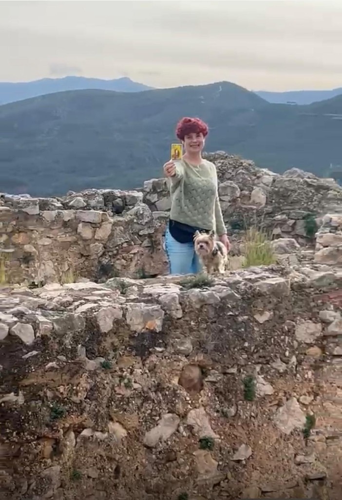 Marisa Le Fay mostrando una carta del tarot en un paisaje de montaña